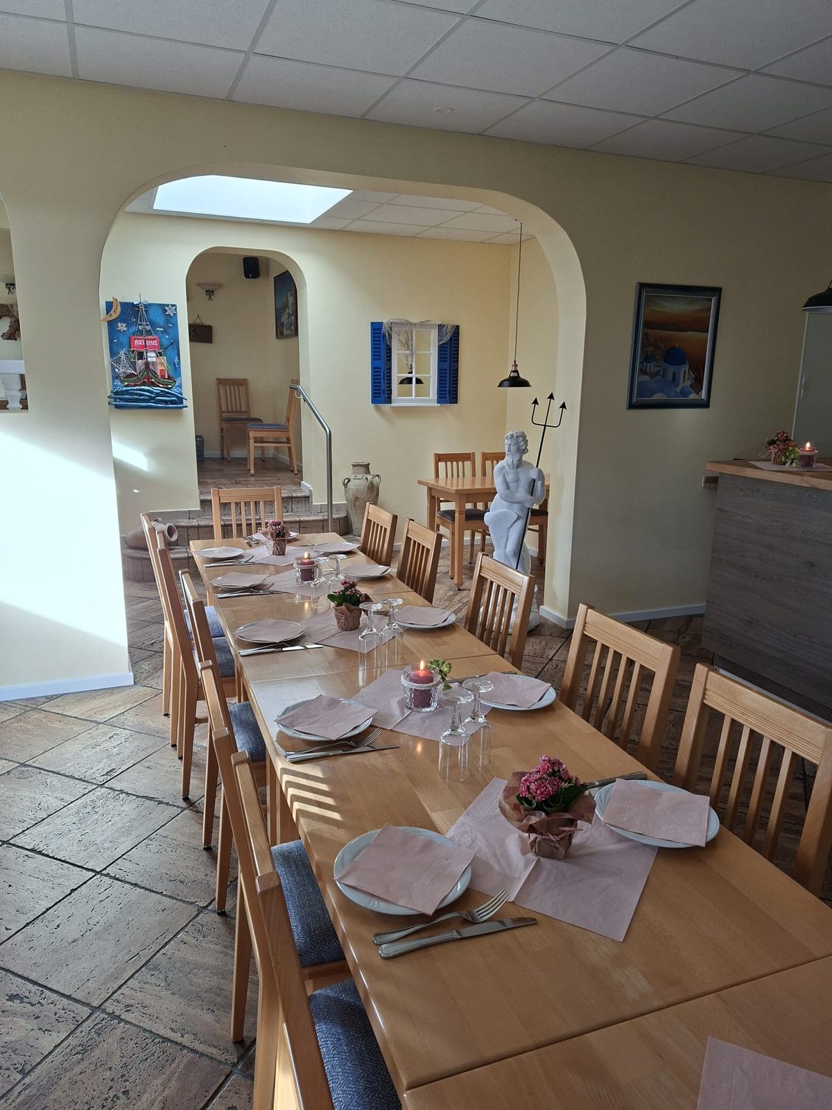 Gedeckte lange Tafel im Gastraum, dahinter Rundbogen, Treppe und Poseidon-Figur